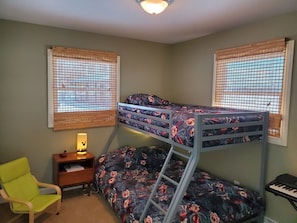 A bunk bed with floral bedding, a desk with a lamp, a chair, and a keyboard on the floor.