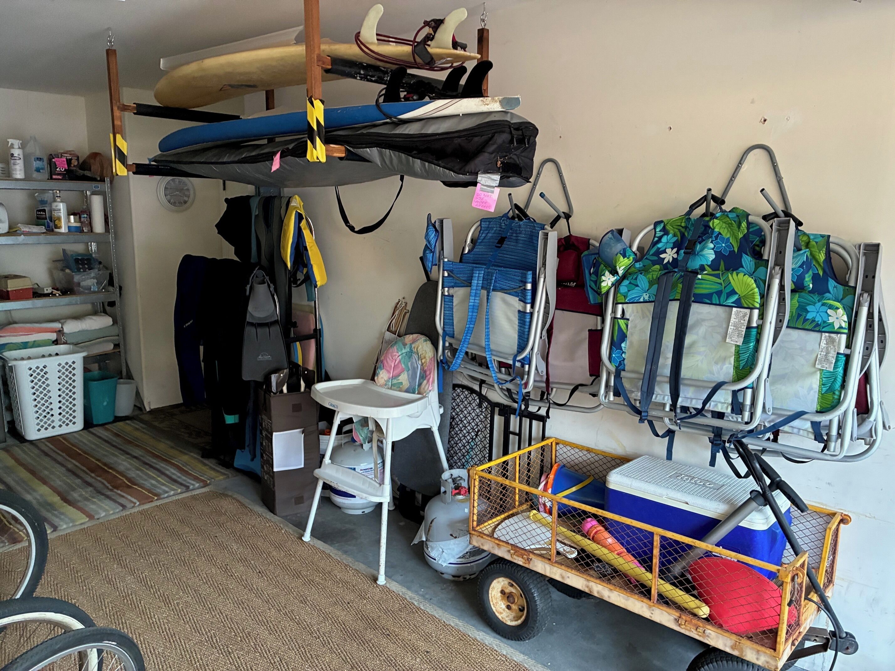 A cluttered storage room with various items including a bunk bed, a baby stroller, a walker, and a cart with a cooler.