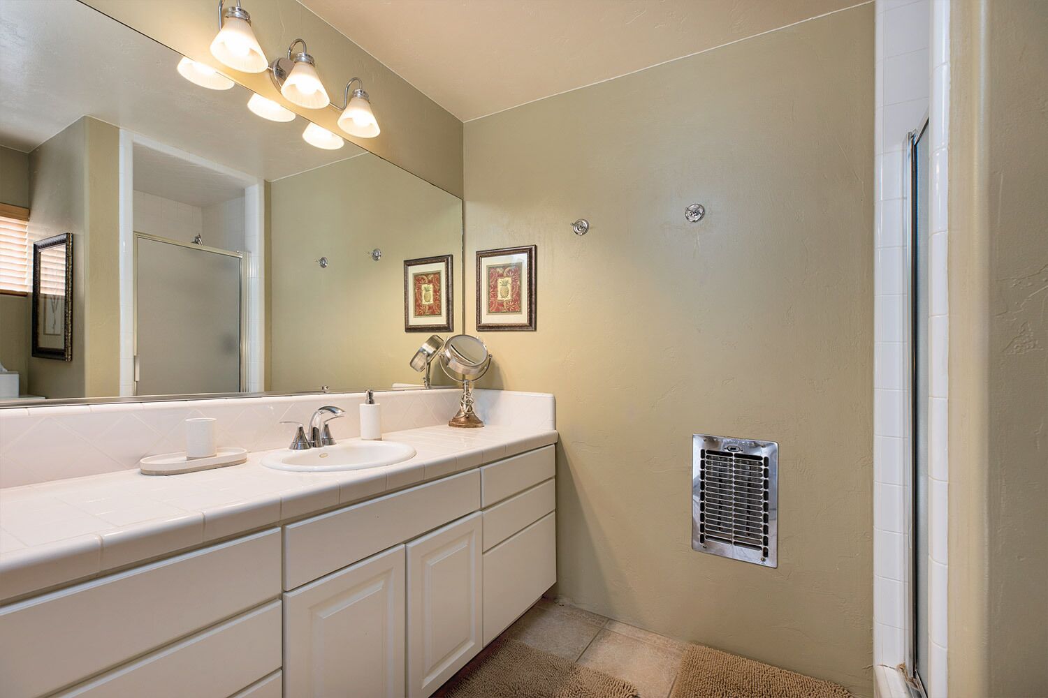 A bathroom with a white vanity, a large mirror, and a wall-mounted heater.