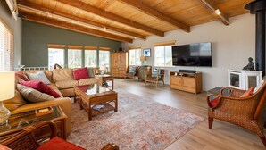 A spacious living room with a high ceiling, wooden beams, a large flat-screen TV, and a fireplace.