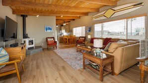 A spacious living area with a high ceiling, wooden beams, a sofa, a coffee table, and a television.