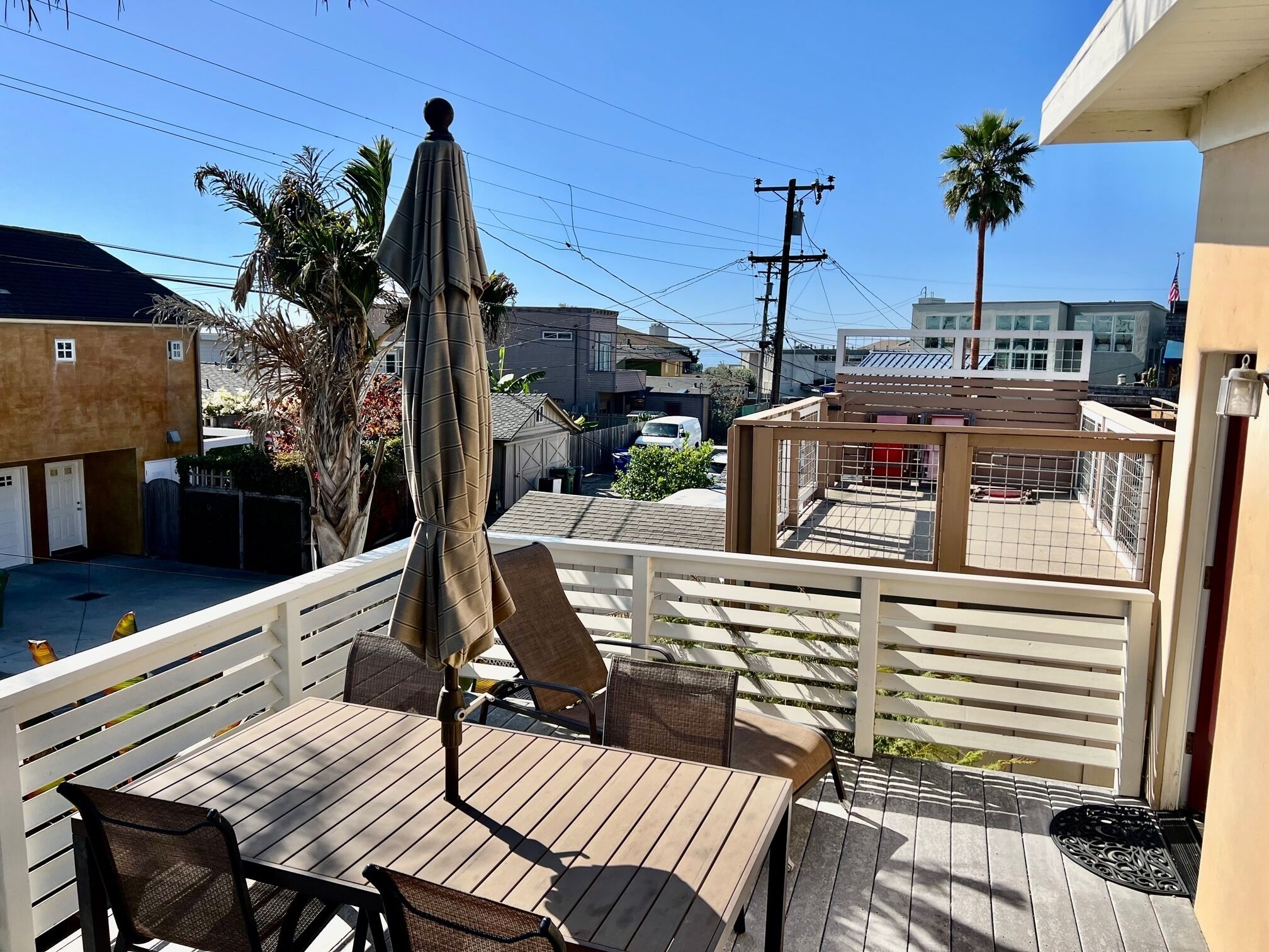 Ein Balkon mit Holztisch und Stühlen, einem Sonnenschirm und Blick auf die Nachbarschaft.