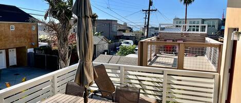 Ein Balkon mit Holztisch und Stühlen, einem Sonnenschirm und Blick auf die Nachbarschaft.