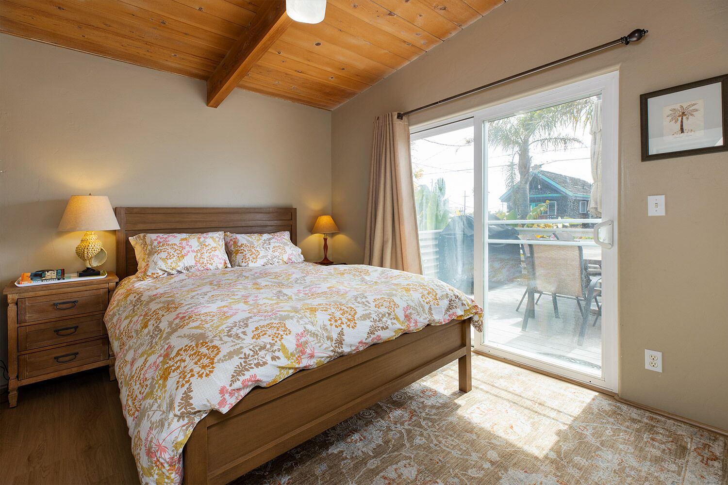 A bedroom with a wooden bed, two bedside lamps, a nightstand, and a large sliding glass door leading to an outdoor area.