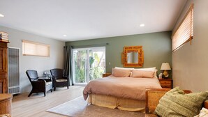 A bedroom with a large bed, a chair, a table, and a view of the outdoors.