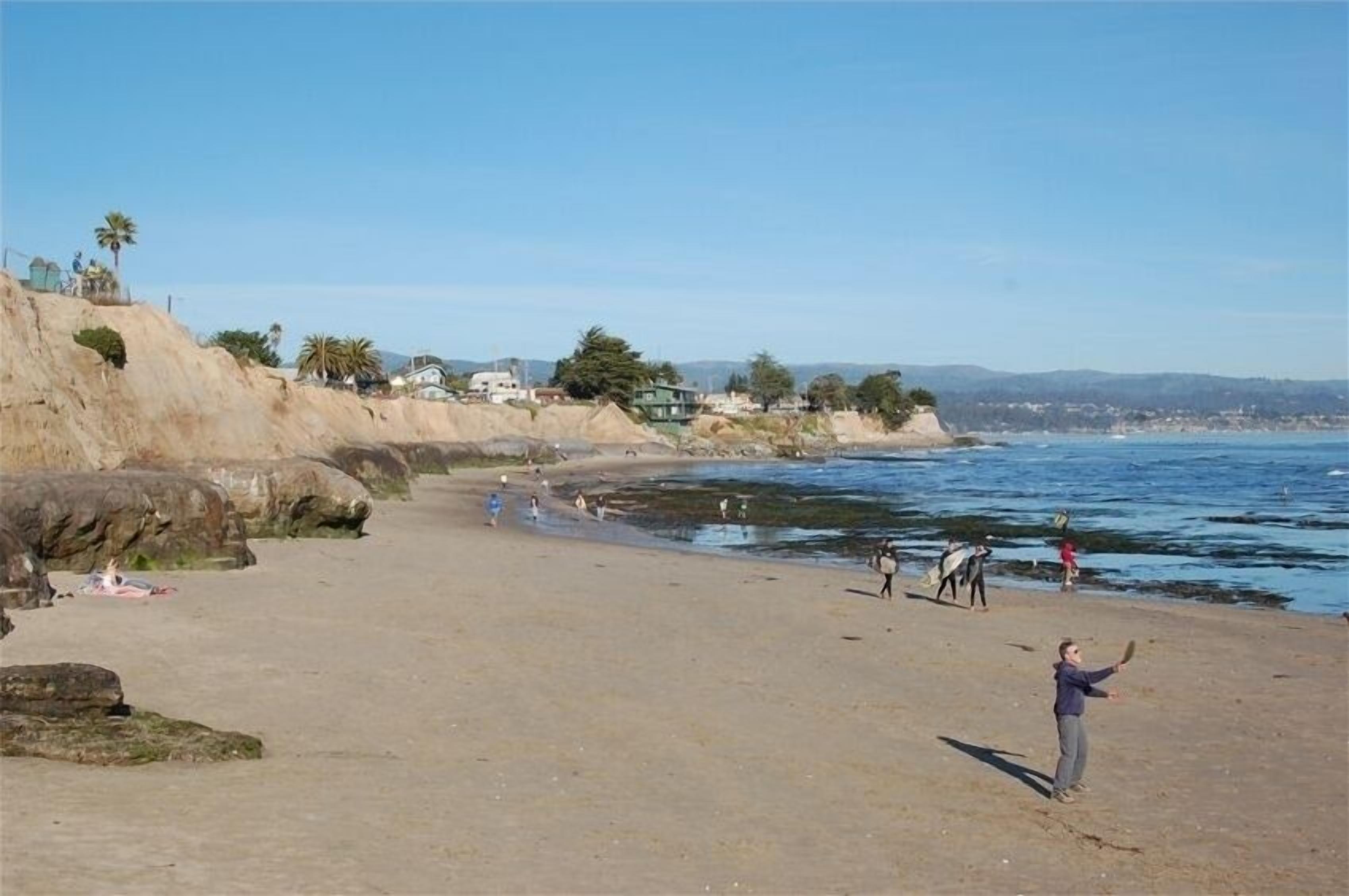 A sandy beach with people, some walking and others standing, near the water.