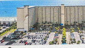 Un grand hôtel à plusieurs étages, doté d’une tour centrale, d’un vaste parking et offrant une vue sur la plage.