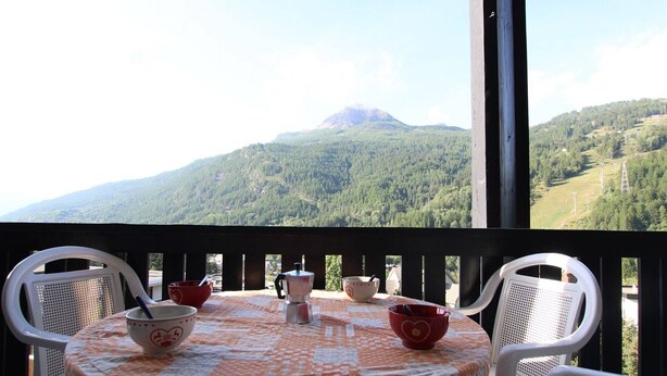A round table with a patterned tablecloth, two white chairs, and three bowls on the balcony overlooking a mountainous landscape. - Cozy Studio in Chantemerle - Sleeps 4, Parking, Balcony, 2 Stars (Saint-Chaffrey)