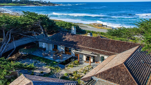 Una casa costera con un patio que da al océano, un pequeño bote amarrado afuera y un puente que conecta con la propiedad.