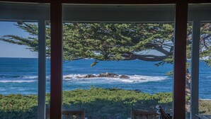Vista desde una ventana con marco de madera, sobre una costa rocosa y el océano.