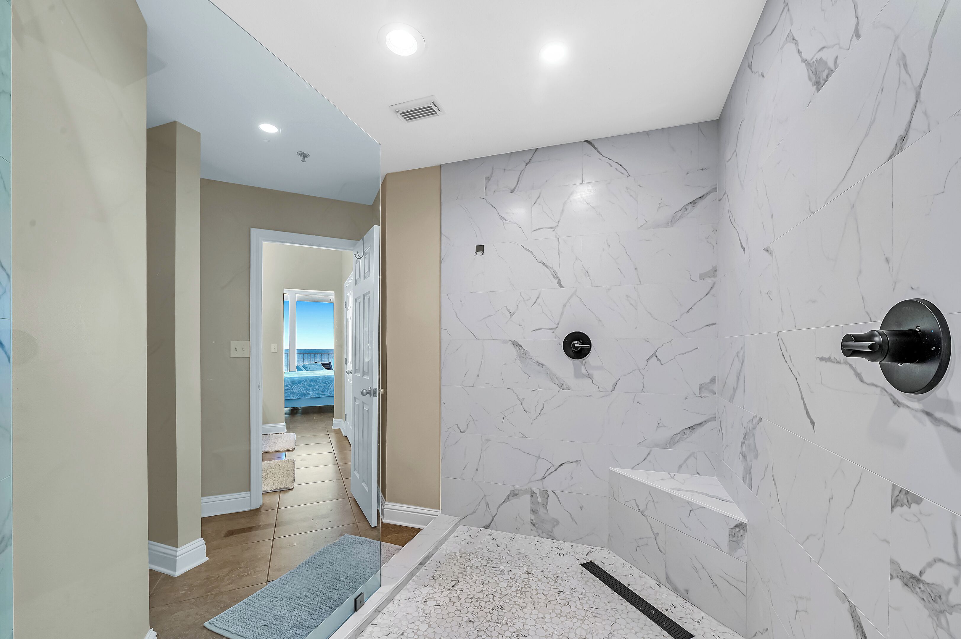 Un baño moderno con paredes de mármol, ducha y una puerta visible que da a otra habitación.