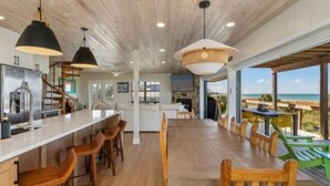 Un comedor amplio con una mesa y sillas de madera, una cocina con encimera blanca y vistas al océano.