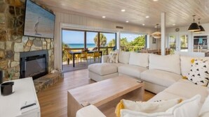 Un salón espacioso con chimenea de piedra, un sofá blanco grande y vistas a la playa.