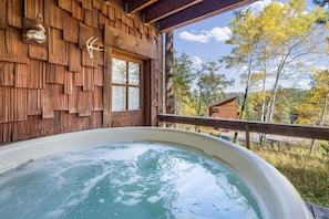 Une cabane en bois avec un jacuzzi, une fenêtre et une vue sur les arbres.