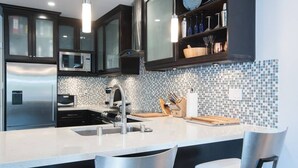 Une cuisine moderne avec des meubles de couleur sombre, un réfrigérateur en acier inoxydable, un four à micro-ondes et un pare-feu en carreaux.
