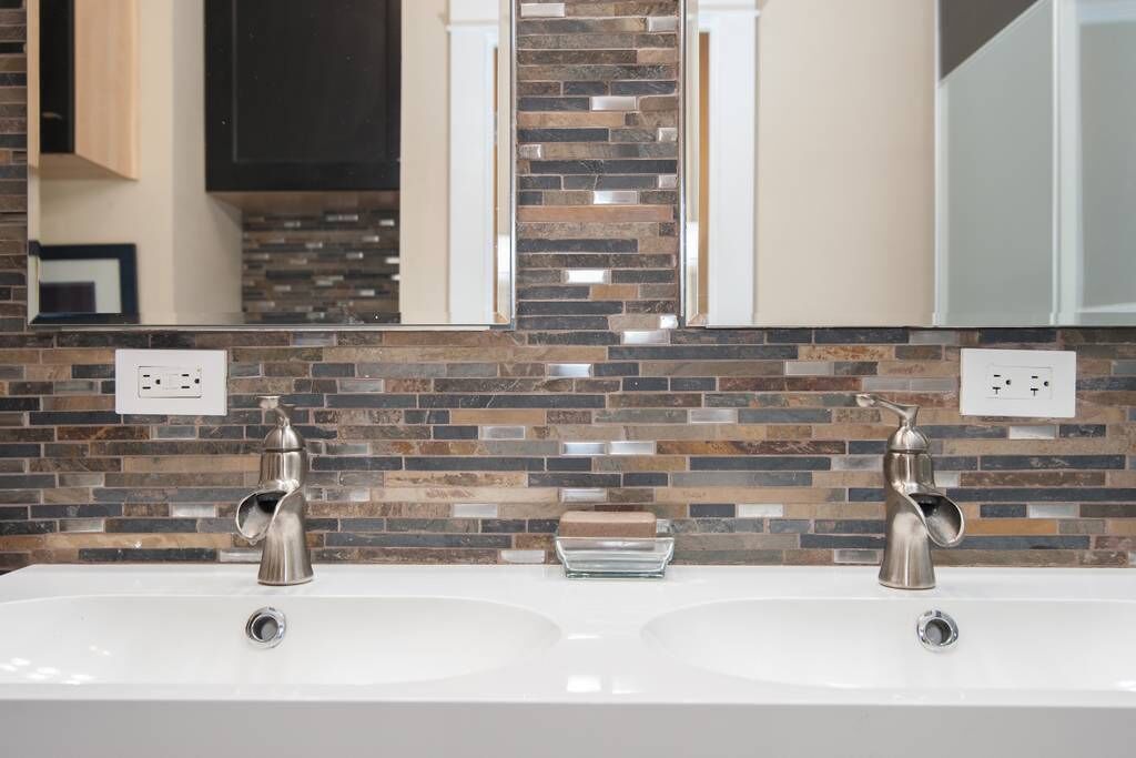 A bathroom with two sinks, a mirror, and a mosaic tile backsplash.