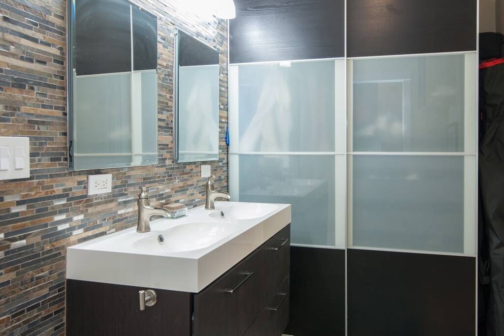 A modern bathroom with a double sink, dark cabinets, and a glass shower enclosure.