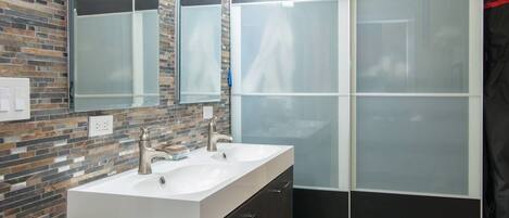 A modern bathroom with a double sink, dark cabinets, and a glass shower enclosure.