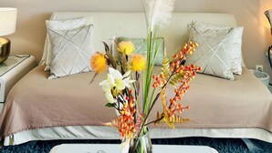 Habitación de hotel con cama, mesita de noche con lámpara y un jarrón decorativo con flores sobre una mesa.