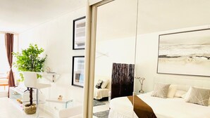 Una habitación de hotel moderna con una cama grande, un escritorio, una silla, una planta y un cuadro en la pared.