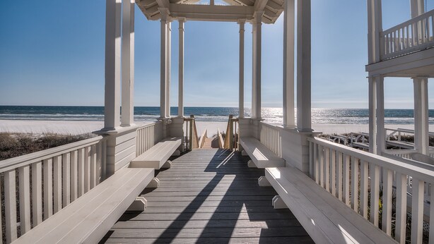 Een houten steiger die naar een strand leidt, met een witte kiosk erbij.