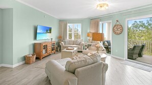 Un salon spacieux doté d’un grand téléviseur à écran plat, de sièges confortables, d’un meuble en bois et d’un balcon aménagé avec du mobilier d’extérieur.