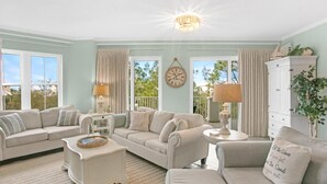 A living room with a beige sofa set, a white side table, a chandelier, and a clock on the wall. - BEACHFRONT BUILDING I PRIVATE BEACH I FREE SEASONAL BEACH SETUP I BLUE MOUNTAIN! (Santa Rosa Beach)