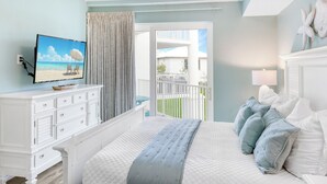 Une chambre à coucher avec un lit, une télévision, une commode et un balcon donnant sur des immeubles.