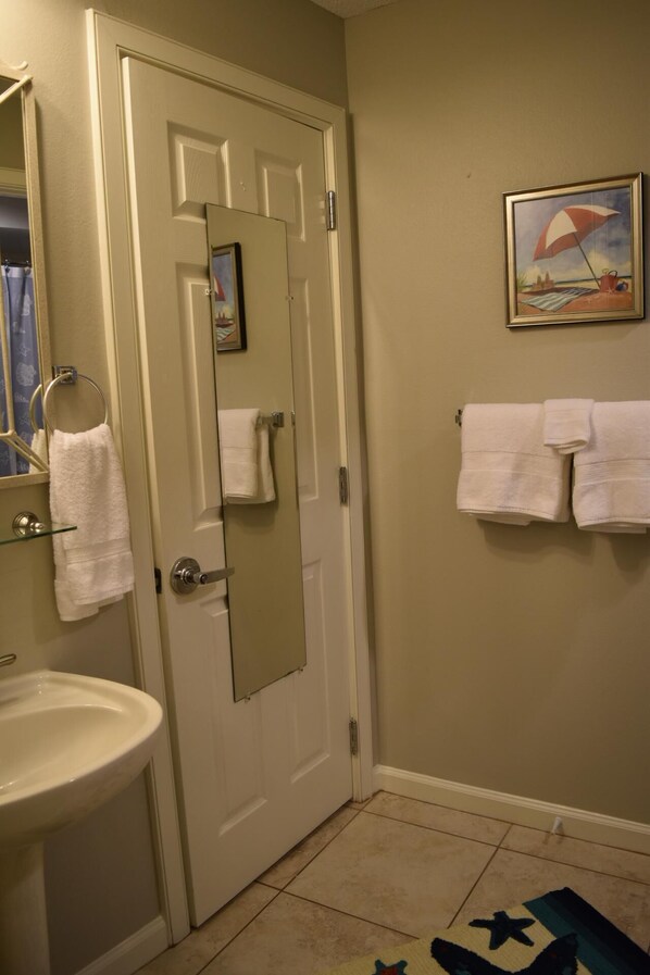 A bathroom with a white sink, a mirror, and a door. There are towels hanging on the wall and a rug on the floor.