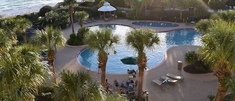 A resort with a pool area, palm trees, and a view of the ocean.