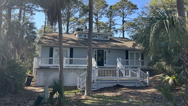 A two-story house with a front porch, surrounded by trees and a clear sky. - 839 Marsh Dunes - Community Pool - Golf Cart Included (Saint Helena Island)
