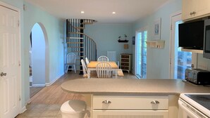 A kitchen with a central island, a dining area with chairs, a staircase, and a TV. - 839 Marsh Dunes - Community Pool - Golf Cart Included (Saint Helena Island)