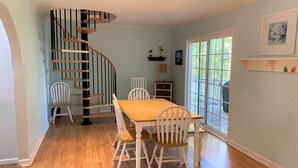 A dining area with a wooden table and chairs, a spiral staircase, and a large window with a view. - 839 Marsh Dunes - Community Pool - Golf Cart Included (Saint Helena Island)