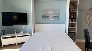 Ein Schlafzimmer mit einem Bett, einem Fernseher, einem Bücherregal und einem Bild an der Wand.