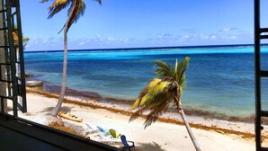 Vista de playa con dos palmeras, un kayak y una silla en la arena.