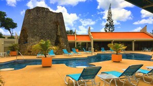 Zona de piscina con sillones de descanso, una gran formación rocosa y un edificio con techo naranja.