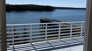 Une vue depuis un balcon donnant sur un lac paisible, avec une terrasse en bois et une balustrade blanche.