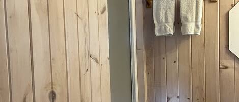 A wooden-paneled bathroom with a shower door, a towel rack with two towels, and a visible vent.