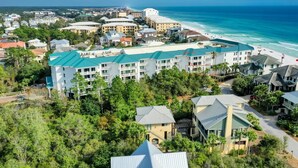 A coastal resort with multiple buildings, including a large hotel with a green roof and a beach view. - BEACHFRONT BUILDING l PRIVATE BEACH l GULF GLIMPSE l SEASONAL BEACH SETUP (Santa Rosa Beach)