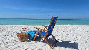 Una sedia da spiaggia con cuscino blu e una borsa di paglia su una spiaggia sabbiosa.