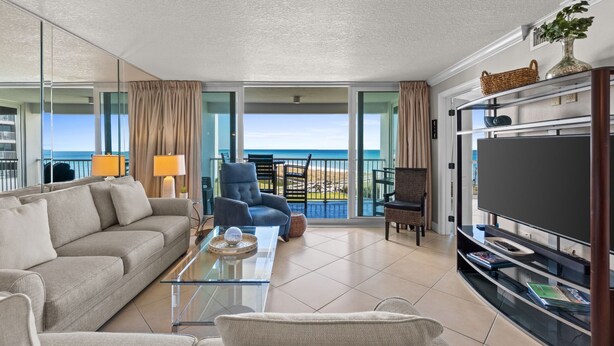 Una camera d'albergo moderna con un balcone vista spiaggia, un divano, una poltrona, una TV e un tavolino da caffè in vetro.