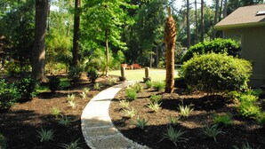 A garden pathway leading to a house with a lawn and trees.
