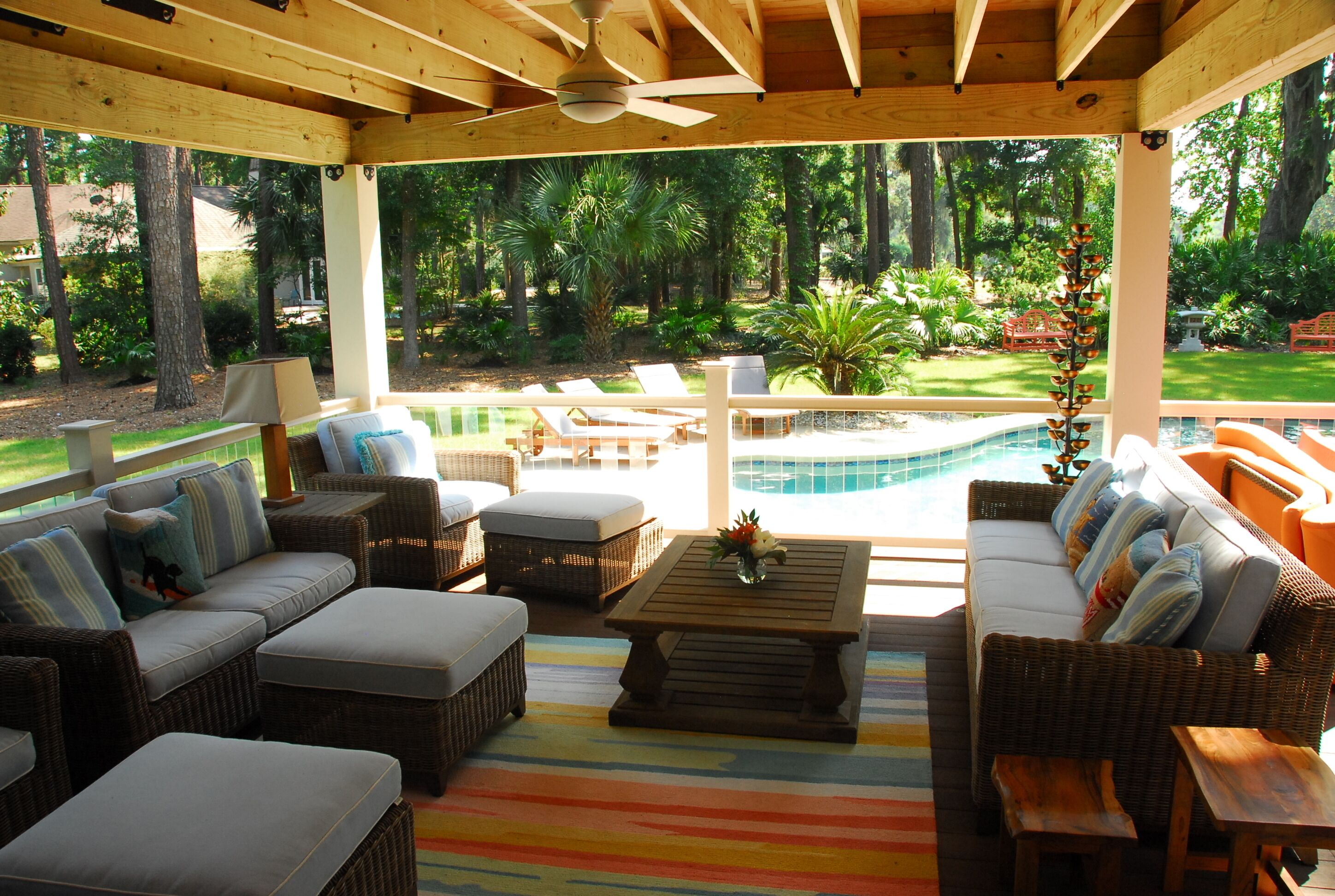 Uma área de varanda externa com móveis de vime, piscina e vista para um jardim exuberante.