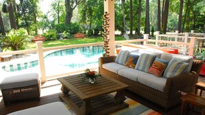 A poolside area with a wicker sofa, a wooden coffee table, and a colorful striped rug.