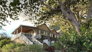 Une maison à deux étages, avec une façade en bois, un balcon et un escalier en pierre menant à l’entrée.
