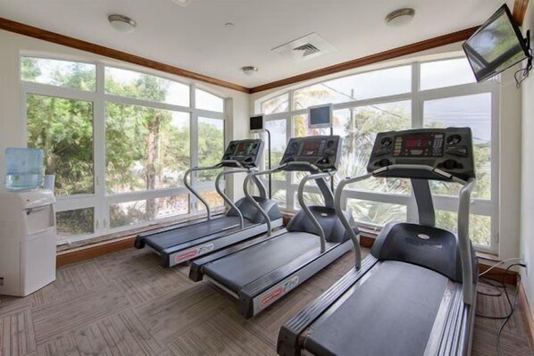 Un gimnasio con cintas de correr, dispensador de agua y ventanas amplias.