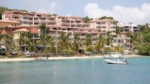 Et strandhotel med flere balkoner, en sandstrand og adskillige både i vandet.