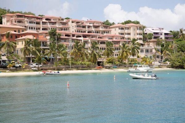 Ein Strandhotel mit mehreren Balkonen, einem Sandstrand und einigen Booten im Wasser.