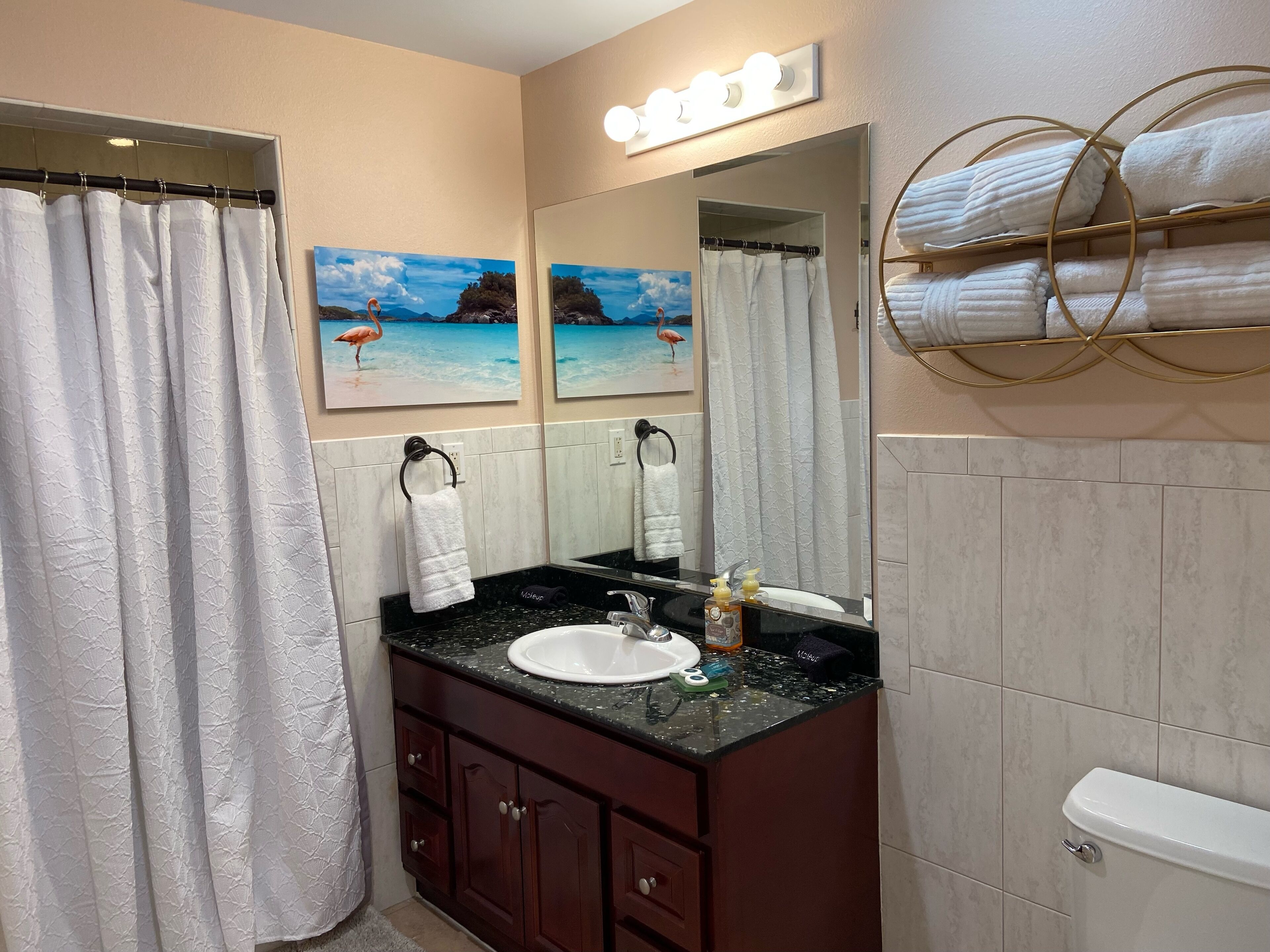 A bathroom with a vanity, a sink, a toilet, a shower curtain, and a towel rack.