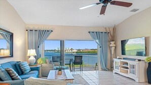 A living room with a sofa, chairs, a coffee table, a TV, and a balcony with a view. - Beautiful Views! Water front! Two Bedrooms and Two Baths with free wifi and beach equipment (Indian Rocks Beach)